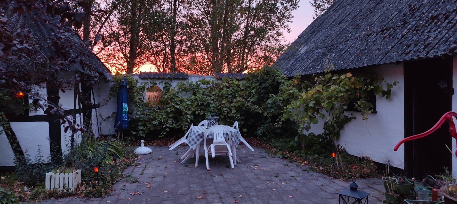 Paved courtyard between white half-timbered farm buildings with a table and chairs at sunset